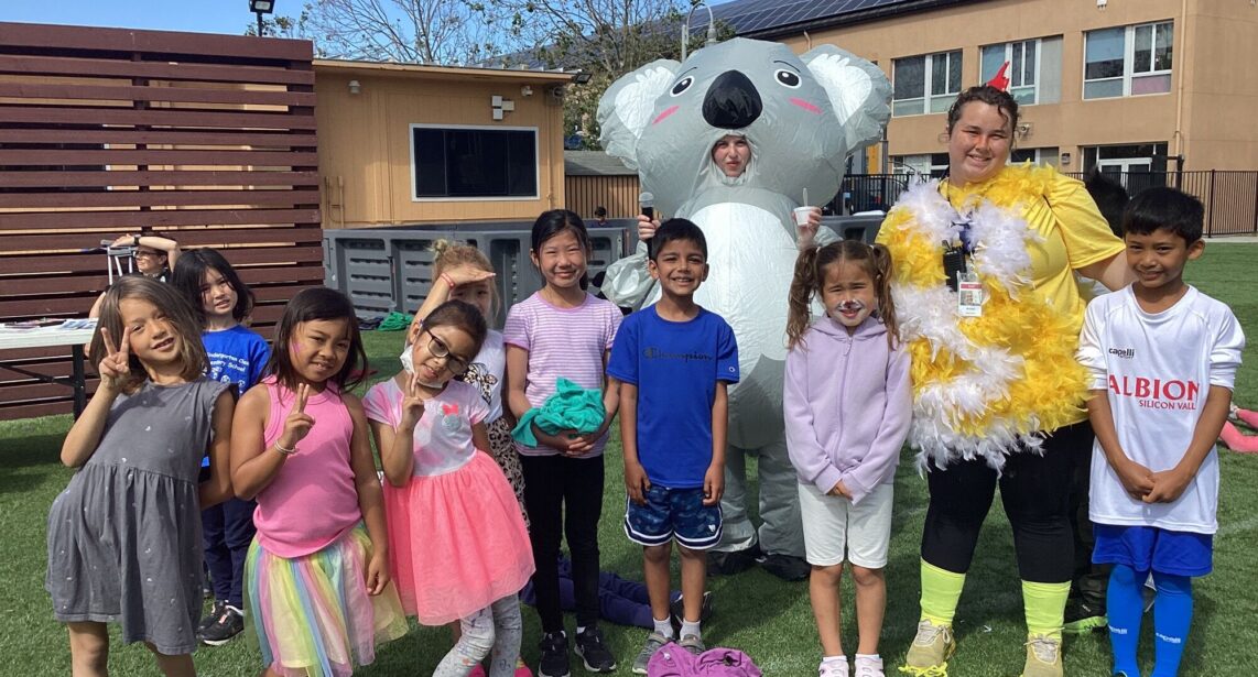 9 kids at summer camp standing outside with counselors dressed in an inflatable koala and chicken costume.
