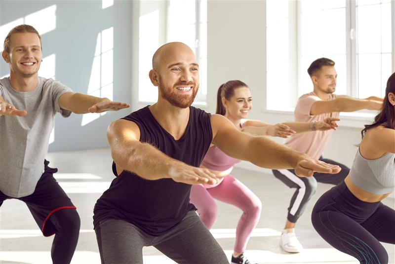Group of adults participating in a group exercise class. They are smiling and doing squats.