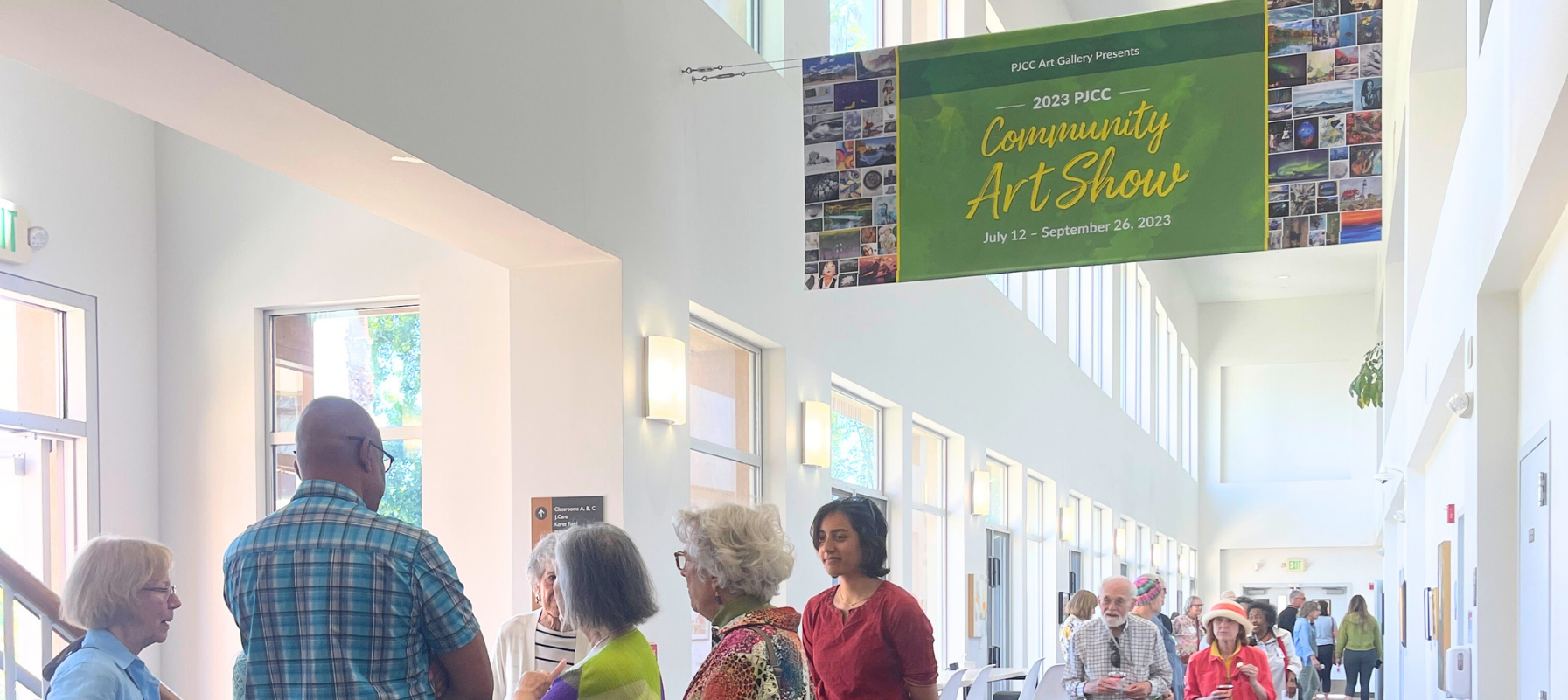 Adults talking in a gallery hallway under a banner for the 2023 Community Art Show