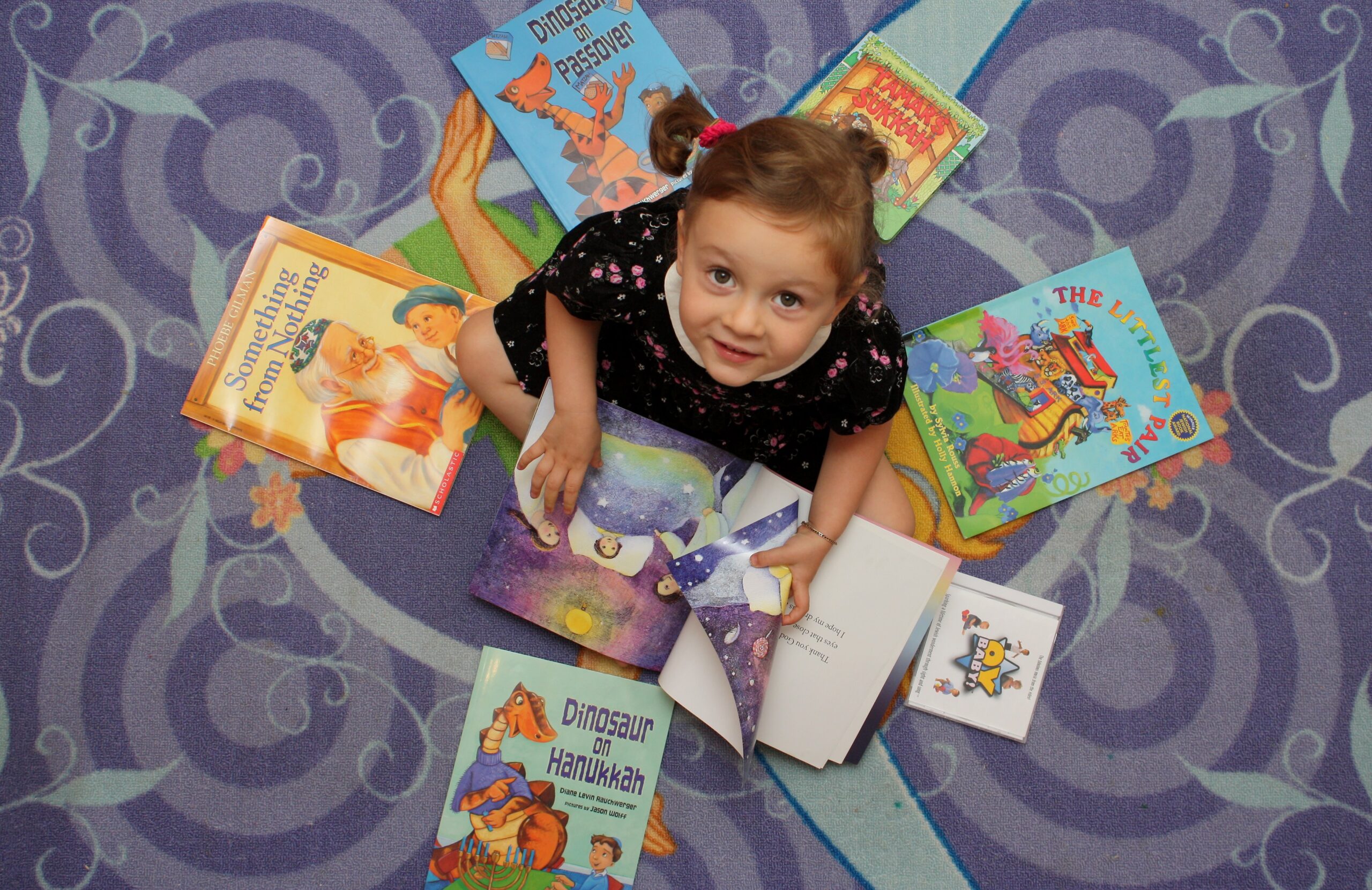 May contain a person sitting on a purple patterned rug, surrounded by books.