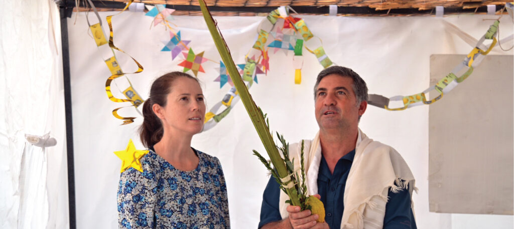 May contain two people celebrating a Jewish holiday, holding branches and fruit.
