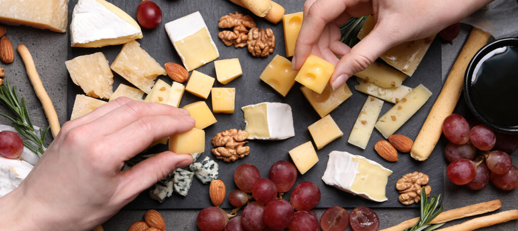 May contain various types of cheese, grapes, nuts, crackers, and a person's hand.